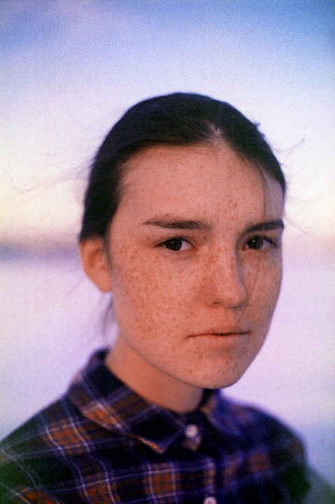 A woman with freckles and dark hair looks directly at the viewer.