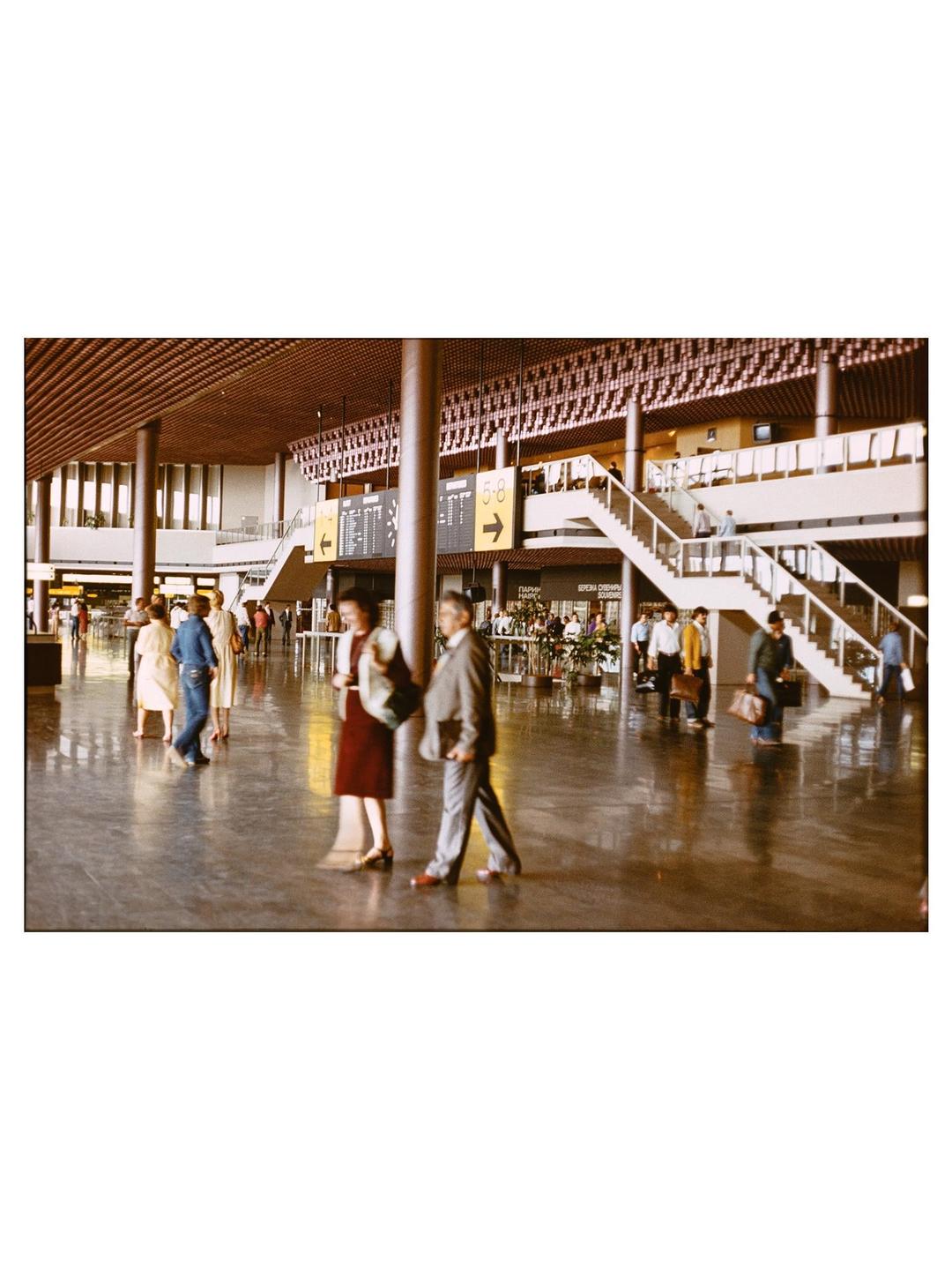People walk through a large, busy airport terminal with high ceilings and multiple levels.