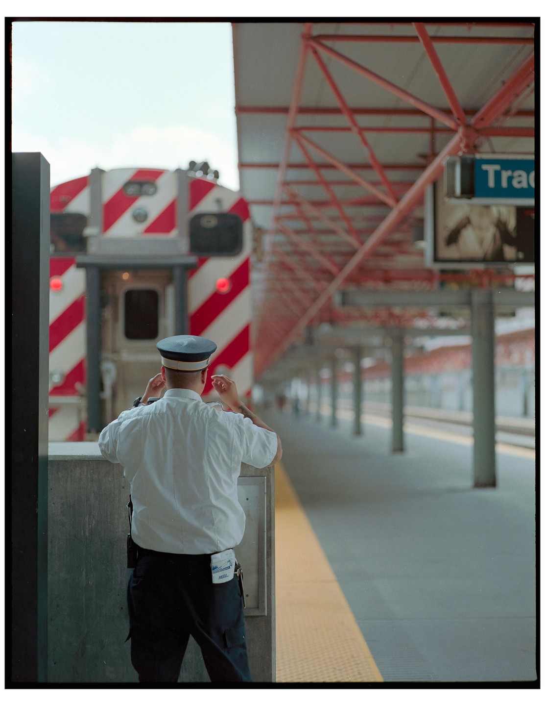 A man in uniform stands on a train platform with a train in the background.