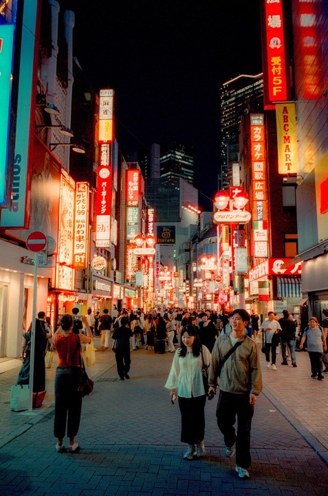 A couple walks down a busy street filled with neon signs and people at night.