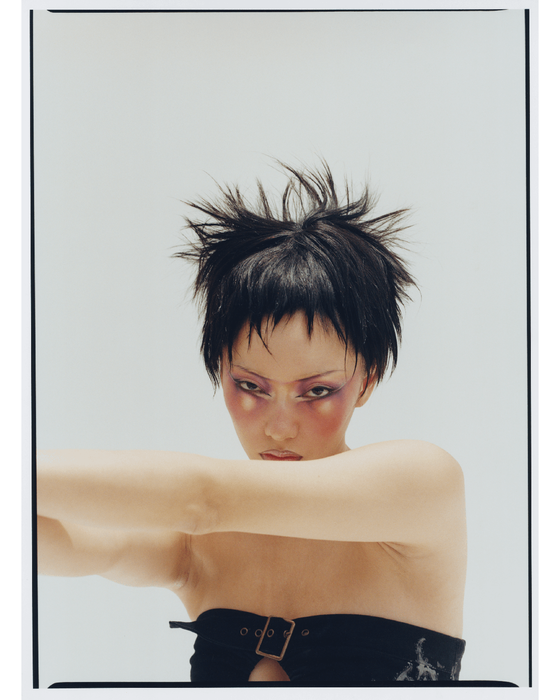 A woman with spiky hair and dramatic makeup poses with her arms crossed in front of her chest.