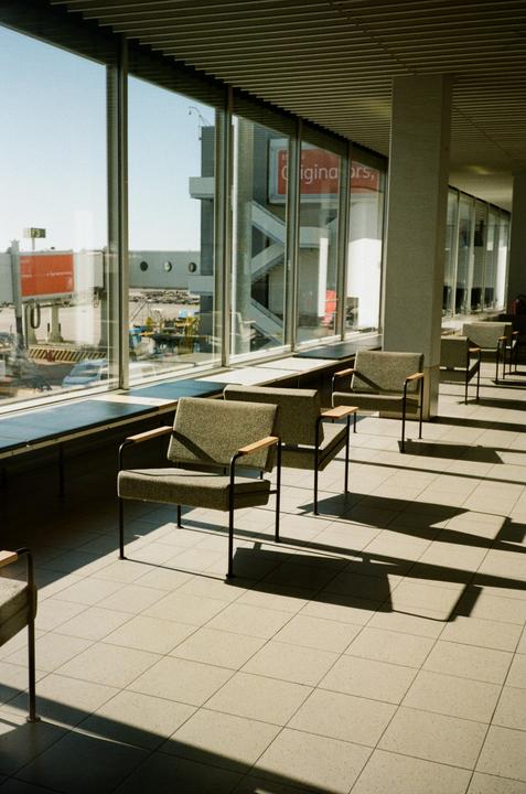 A row of empty chairs sits in front of a large window overlooking an airport tarmac.