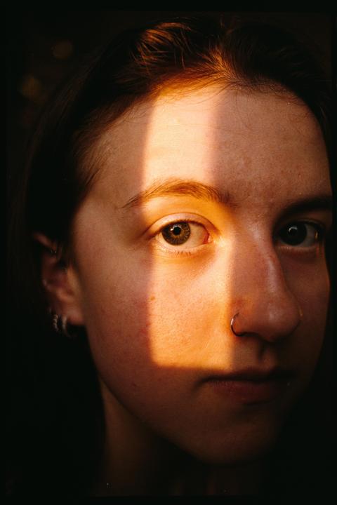 A woman's face is illuminated by a strong beam of light, creating a shadow across her nose and one eye.