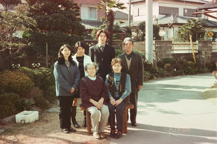 A family of six poses for a group portrait outdoors in front of a house and garden.