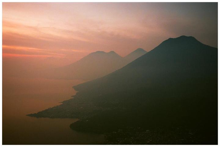 A hazy sunset over a lake with mountains and a town along the shore.