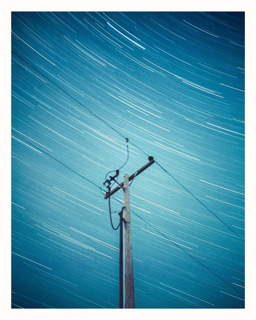 A utility pole stands against a night sky filled with star trails.