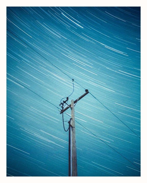 A utility pole stands against a night sky filled with star trails.