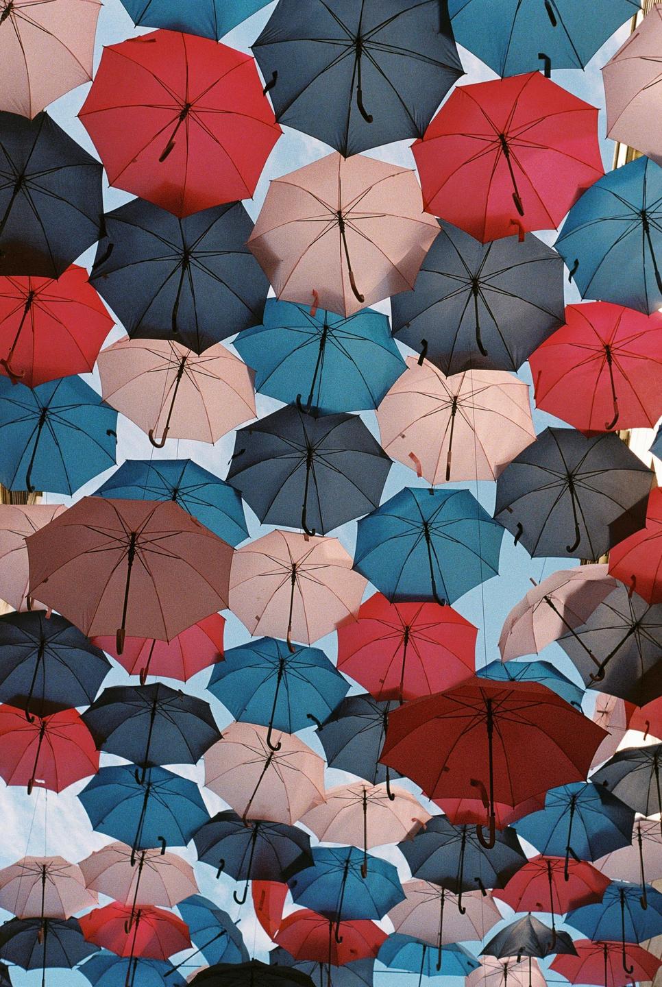 Many colorful umbrellas are suspended in the air against a bright sky.