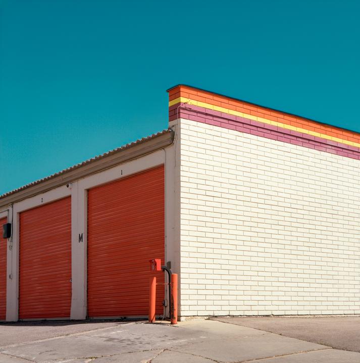 A white brick building with orange garage doors and a colorful striped roofline stands under a clear blue sky.