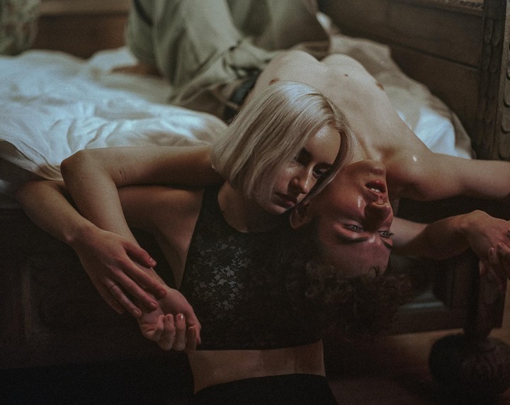 A woman with blonde hair rests her head on a man with curly hair, both lying down.