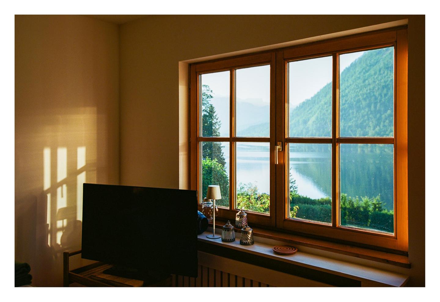 Sunlight streams through a window, illuminating a room with a television and a view of a lake and mountains.