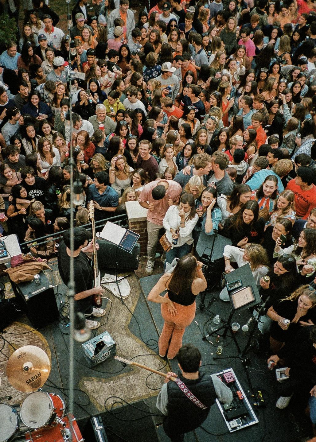 A large crowd of people watches a band perform on a stage.