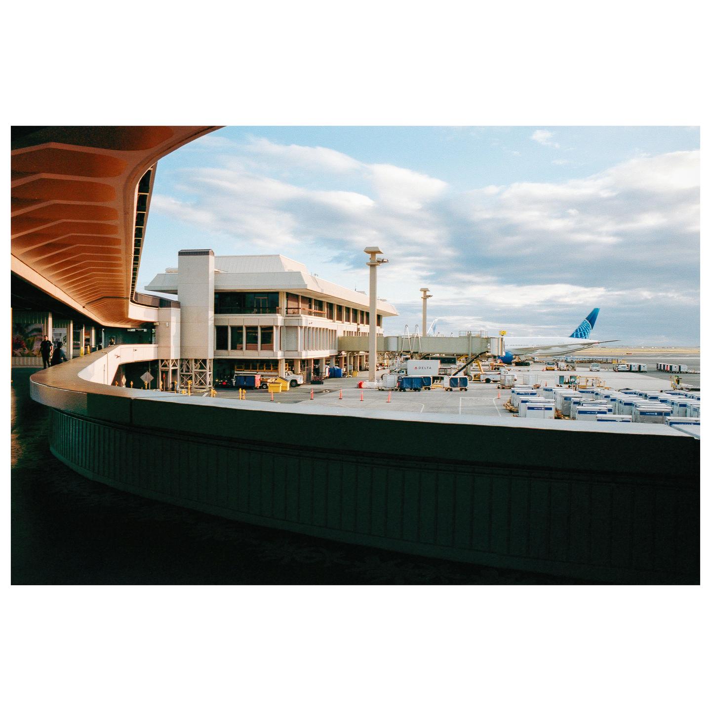 An airplane is parked at an airport gate next to a terminal building under a cloudy sky.