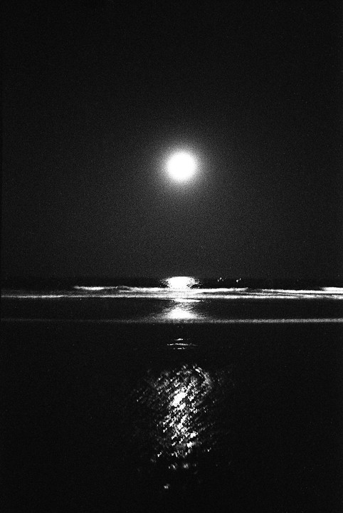 The moon is reflected on the surface of the ocean at night.