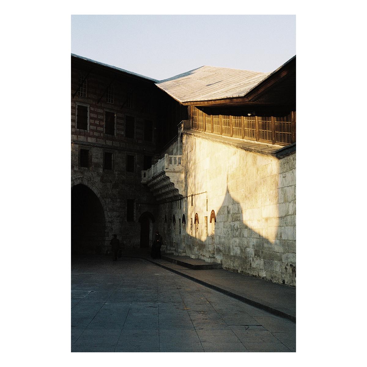 A street in Istanbul is illuminated by the golden hour sun, casting a large shadow on a stone wall.