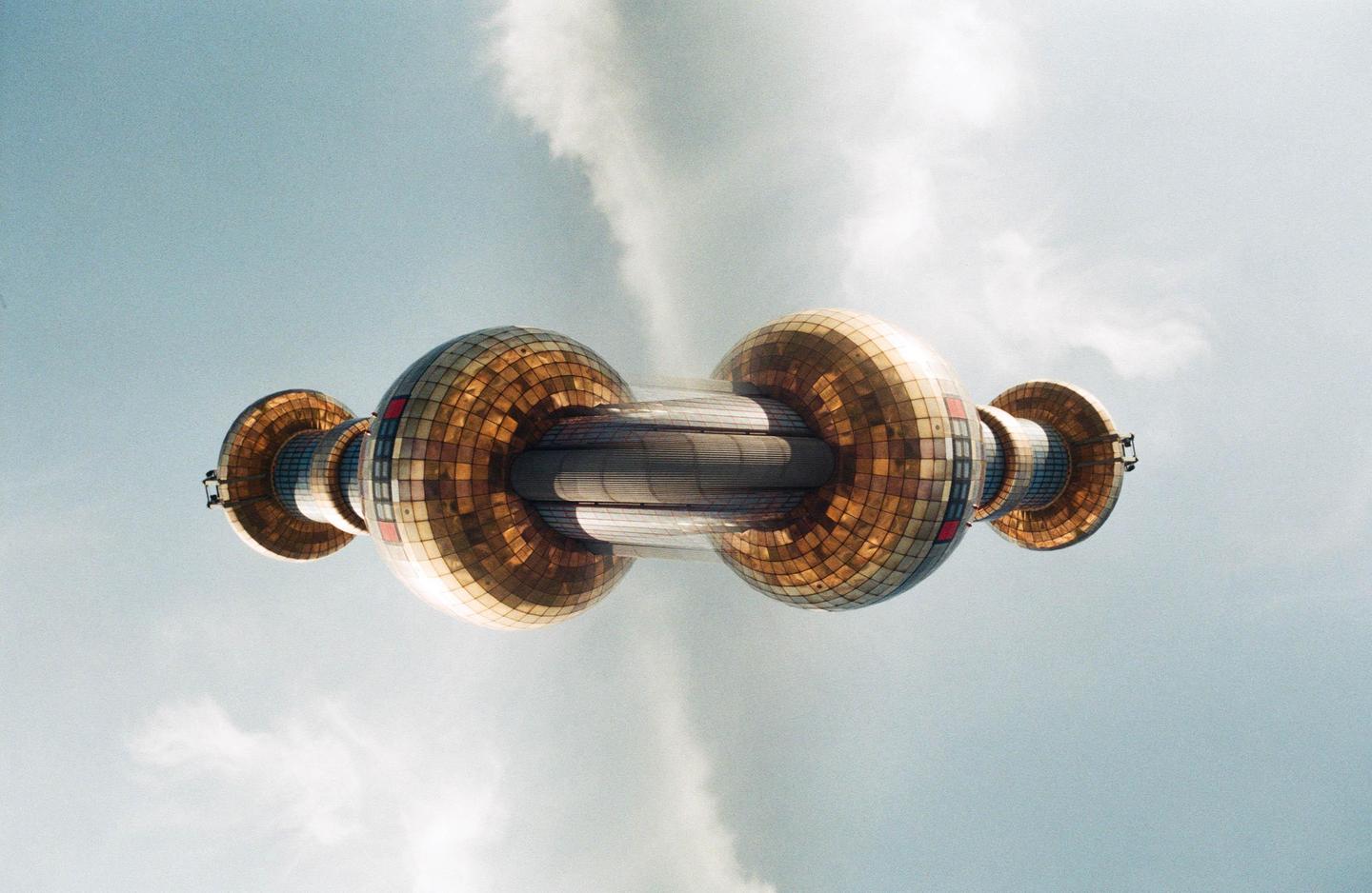 A double exposure shows a mirrored image of the Spittelau incinerator against a cloudy sky.