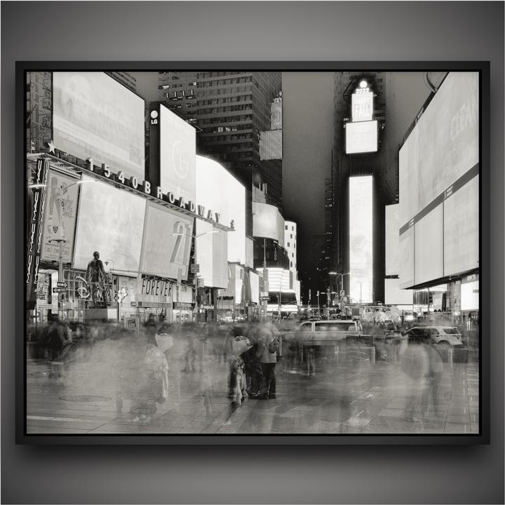 A long exposure shot of Times Square at night shows blurred people and vehicles moving past brightly lit billboards.