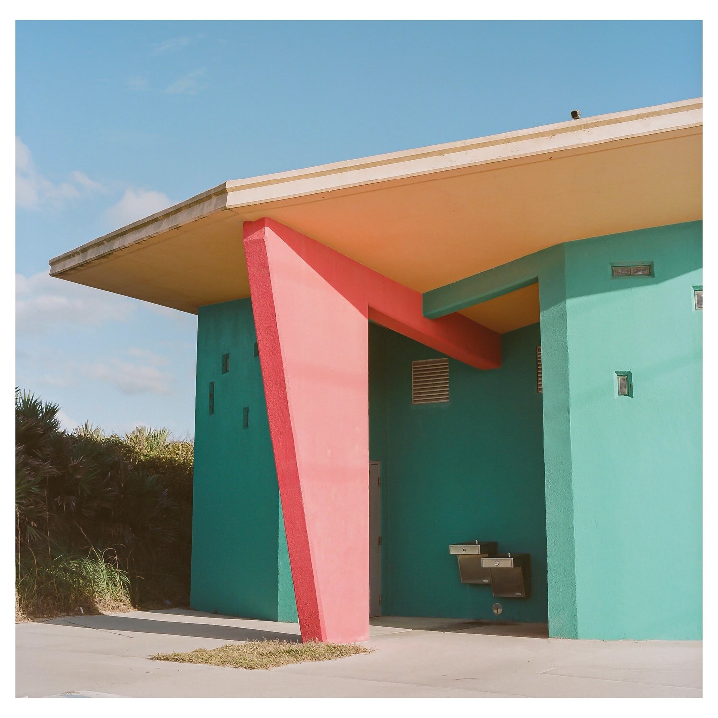 A teal building with a coral support beam and a yellow ceiling stands under a clear blue sky.
