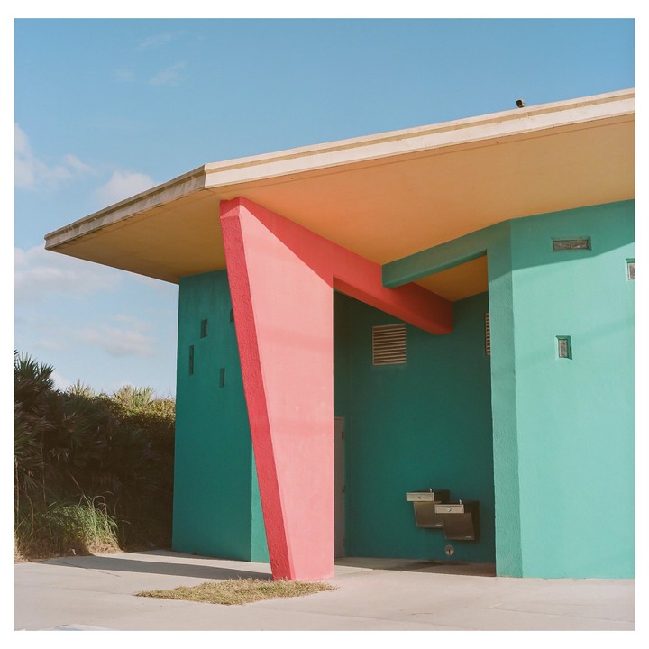 A teal building with a coral support beam and a yellow ceiling stands under a clear blue sky.