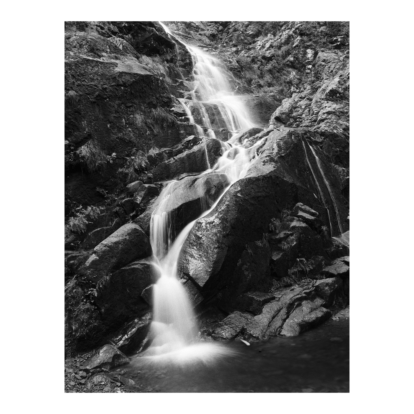 A long exposure shot captures the smooth flow of a waterfall cascading over dark rocks into a pool below.