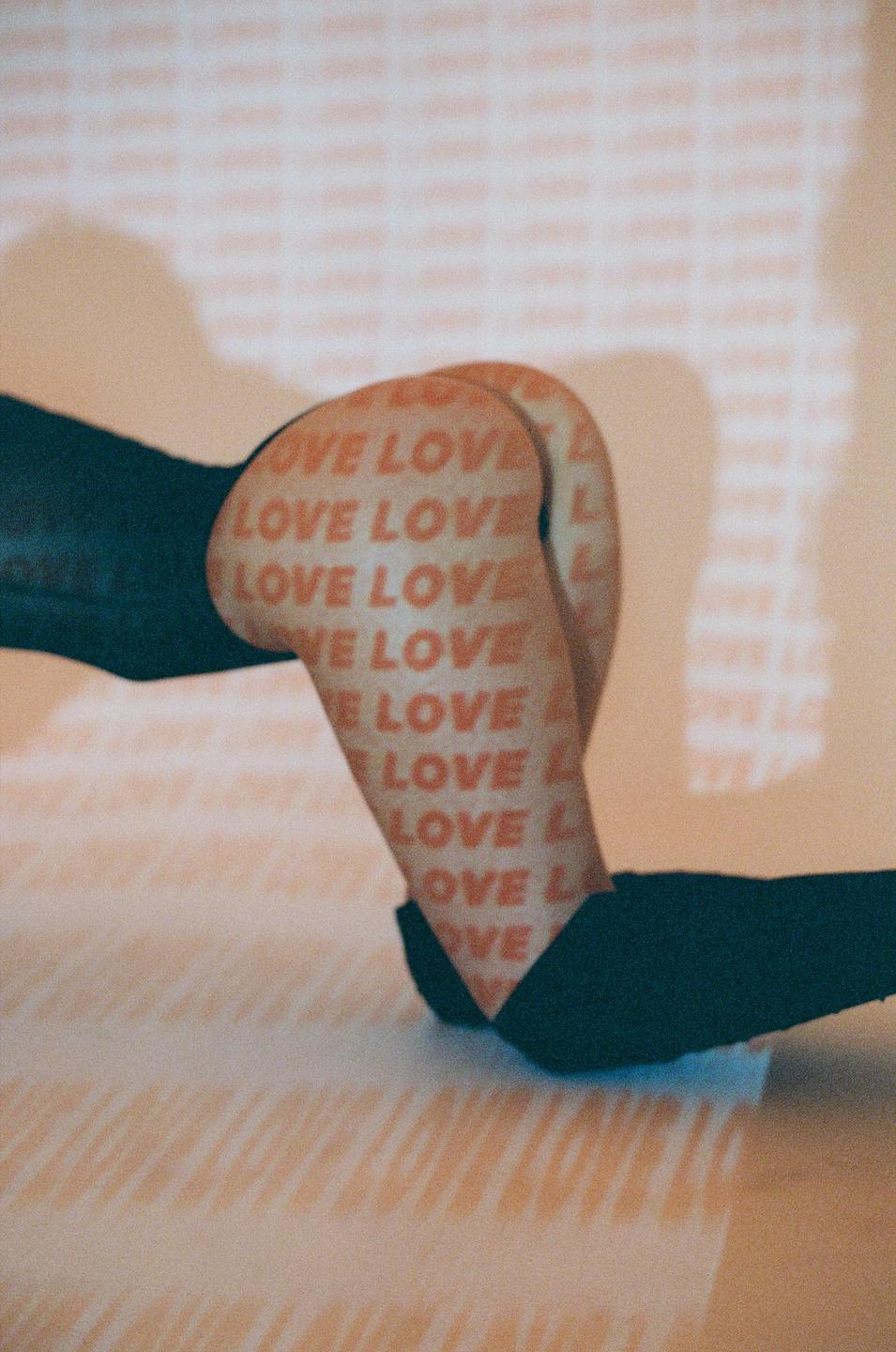 A person is on their hands and knees with the word "LOVE" projected onto their legs and the wall.