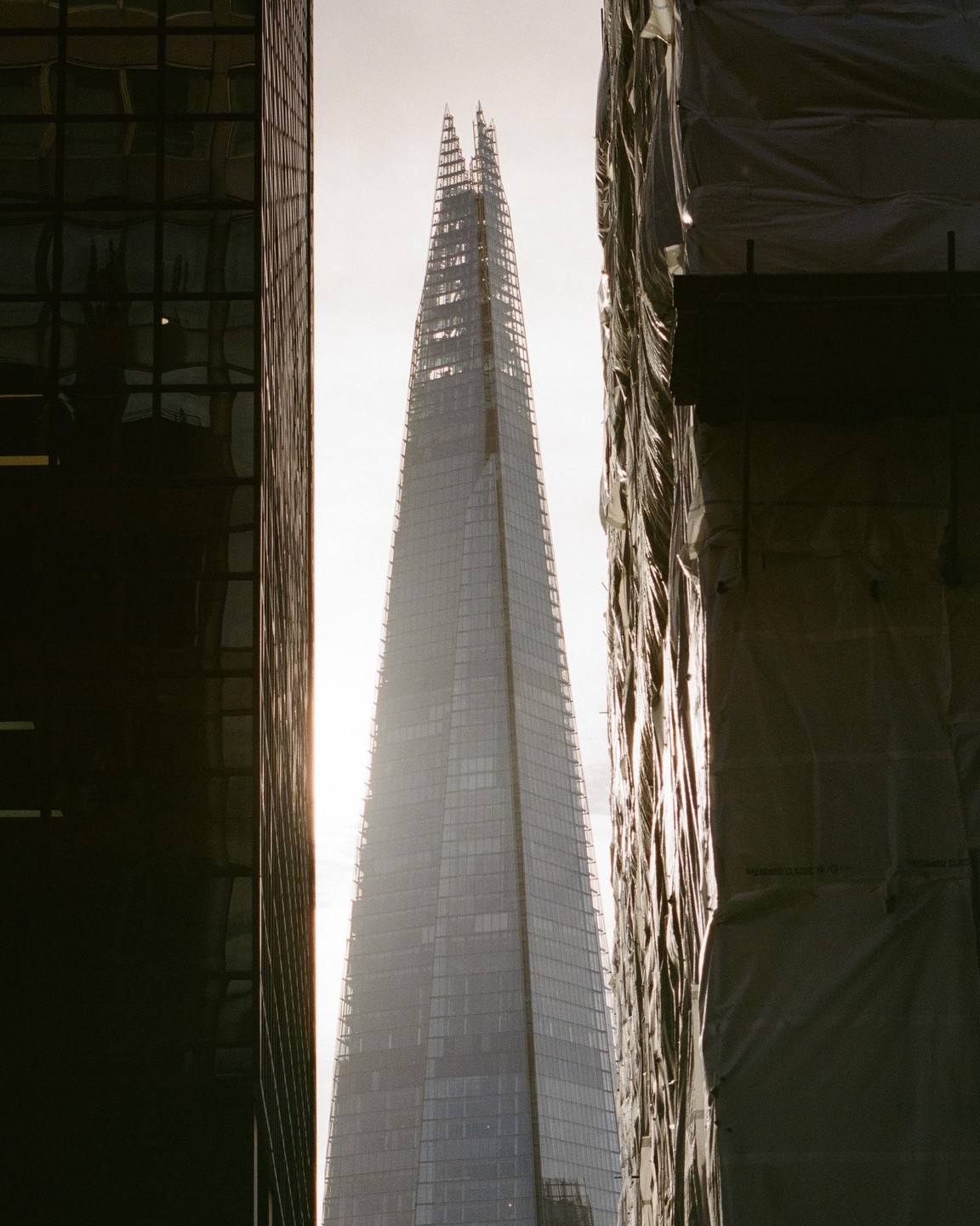 The Shard skyscraper rises between two other buildings, one dark and reflective, the other covered in scaffolding.