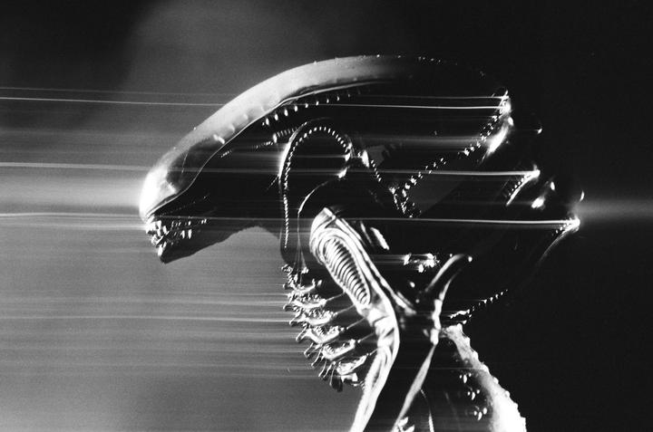 A black and white image shows a creature with an elongated head and visible teeth, with horizontal light streaks across the frame.