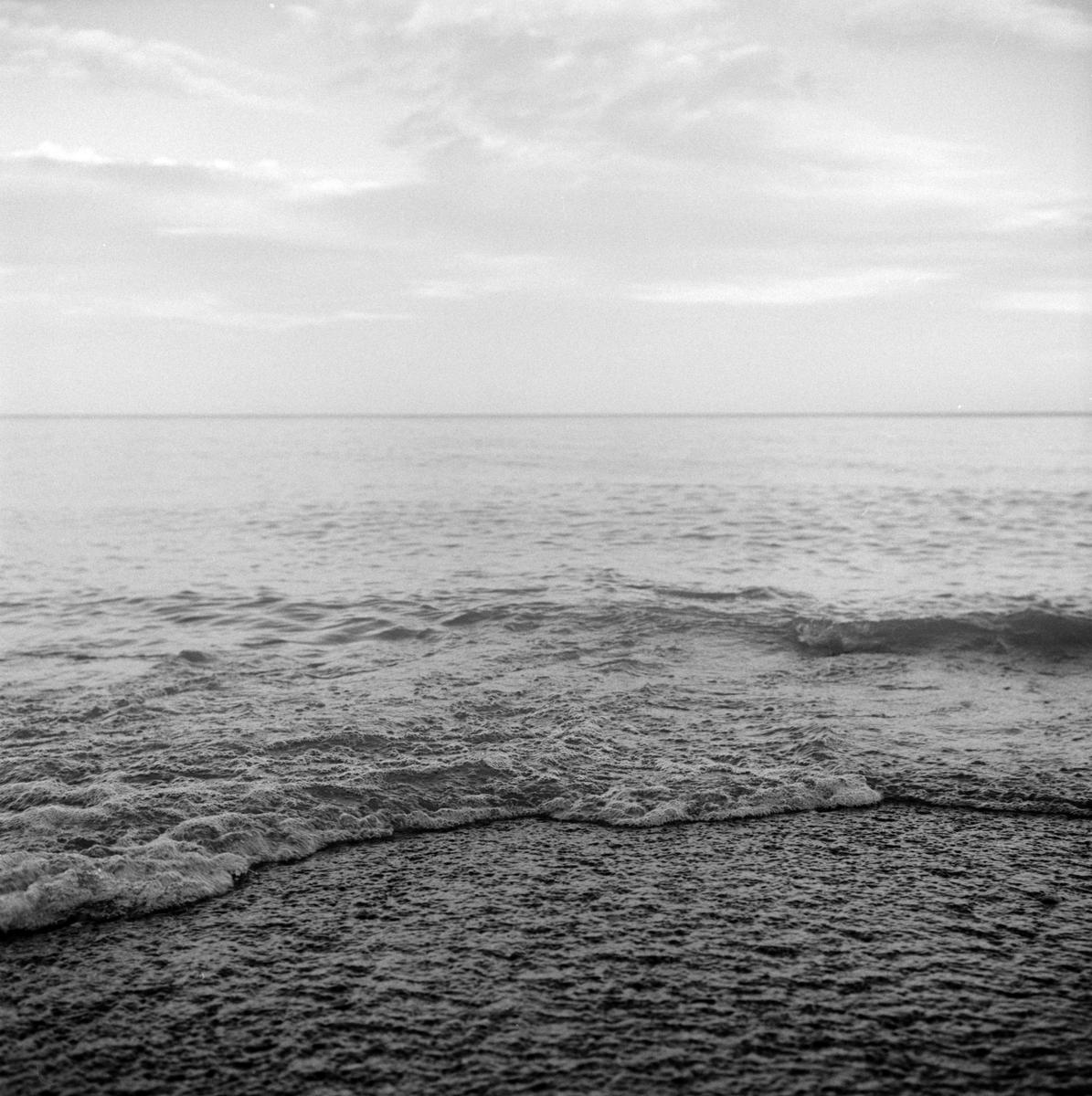 Waves break on a beach under a cloudy sky.