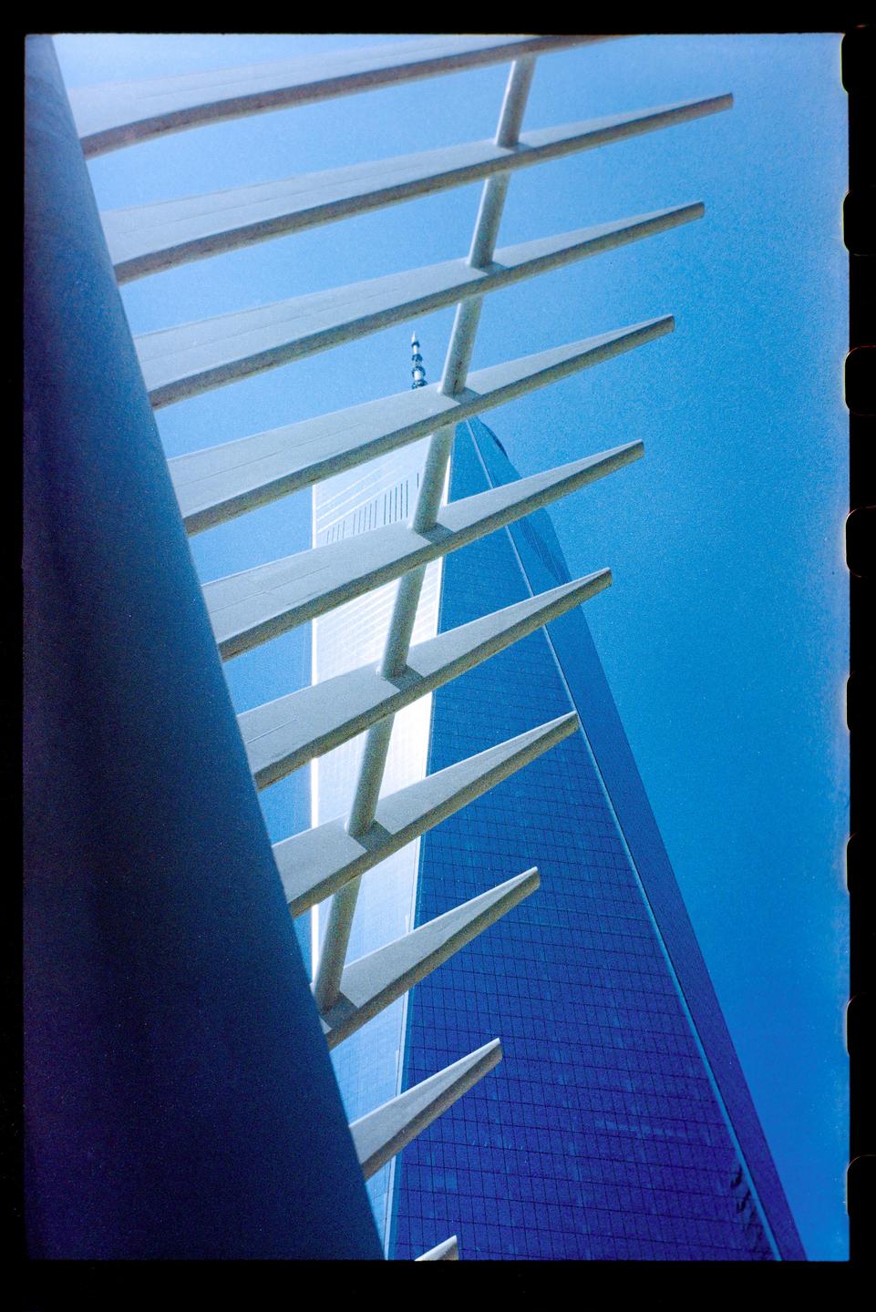 A blue skyscraper is visible through a white architectural structure against a clear blue sky.