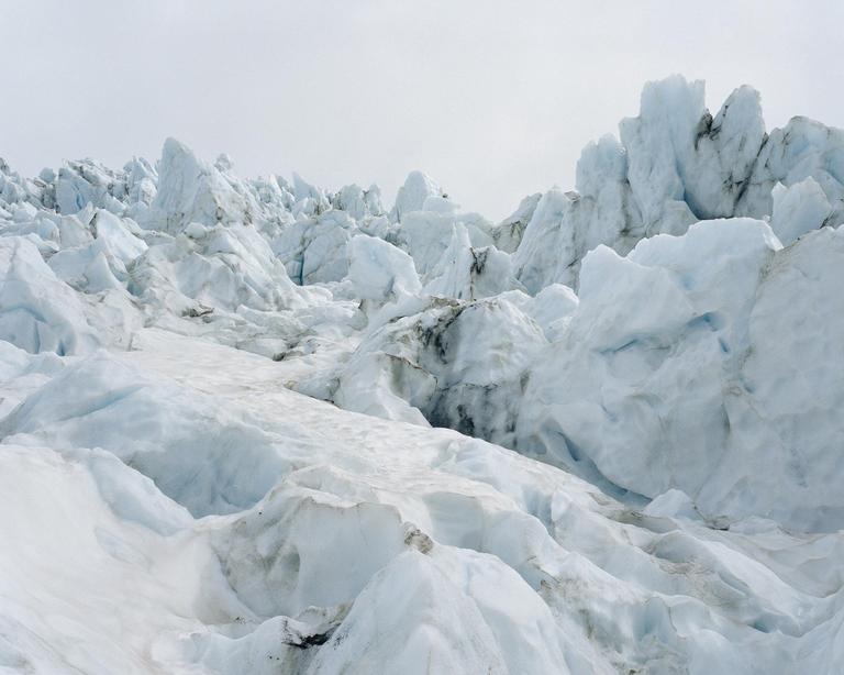 A vast expanse of a glacier with jagged ice formations and snow is visible under a bright sky.