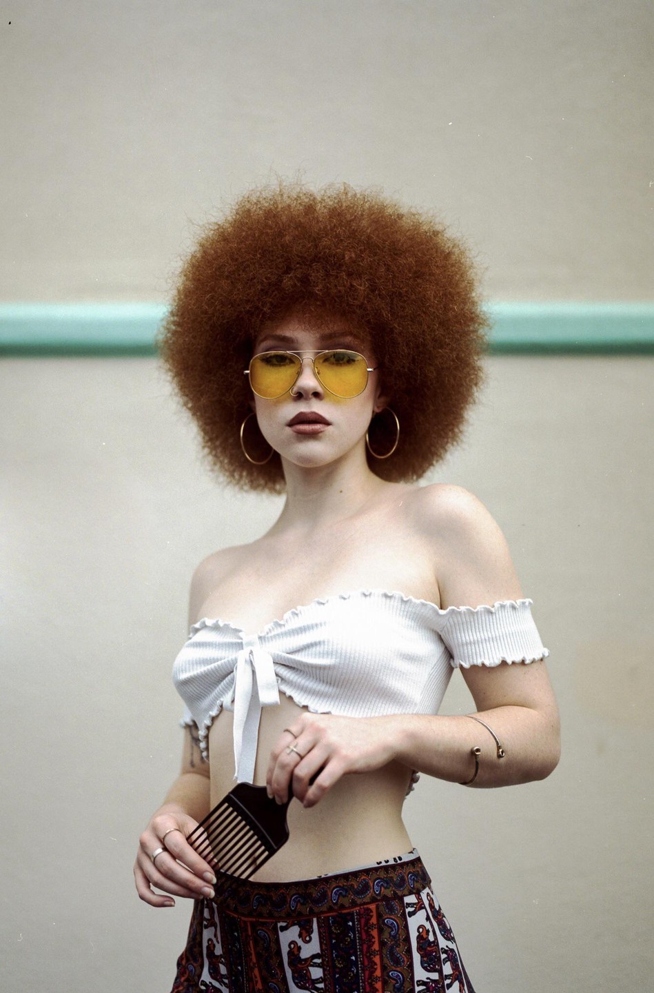 A woman with an afro and yellow sunglasses holds a hair pick.