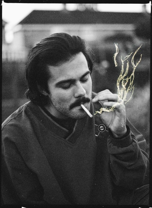A man with a mustache smokes a cigarette with etched smoke.
