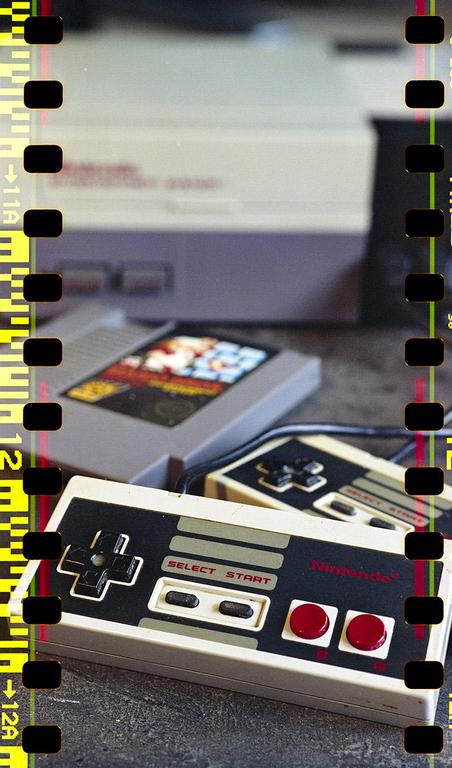 A Nintendo Entertainment System console, game cartridge, and two controllers are arranged on a dark surface.