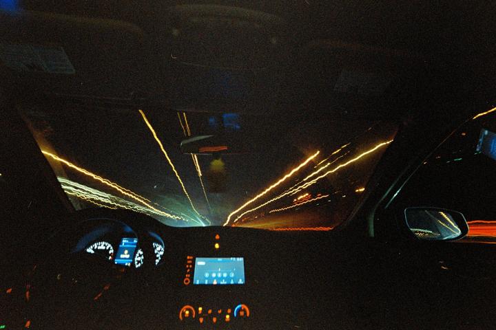 The interior of a car is visible at night with light trails from other vehicles on the road.