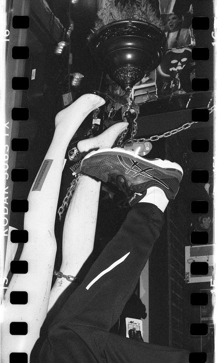 A person's leg and two mannequin legs are chained together and hang upside down from a ceiling fixture.
