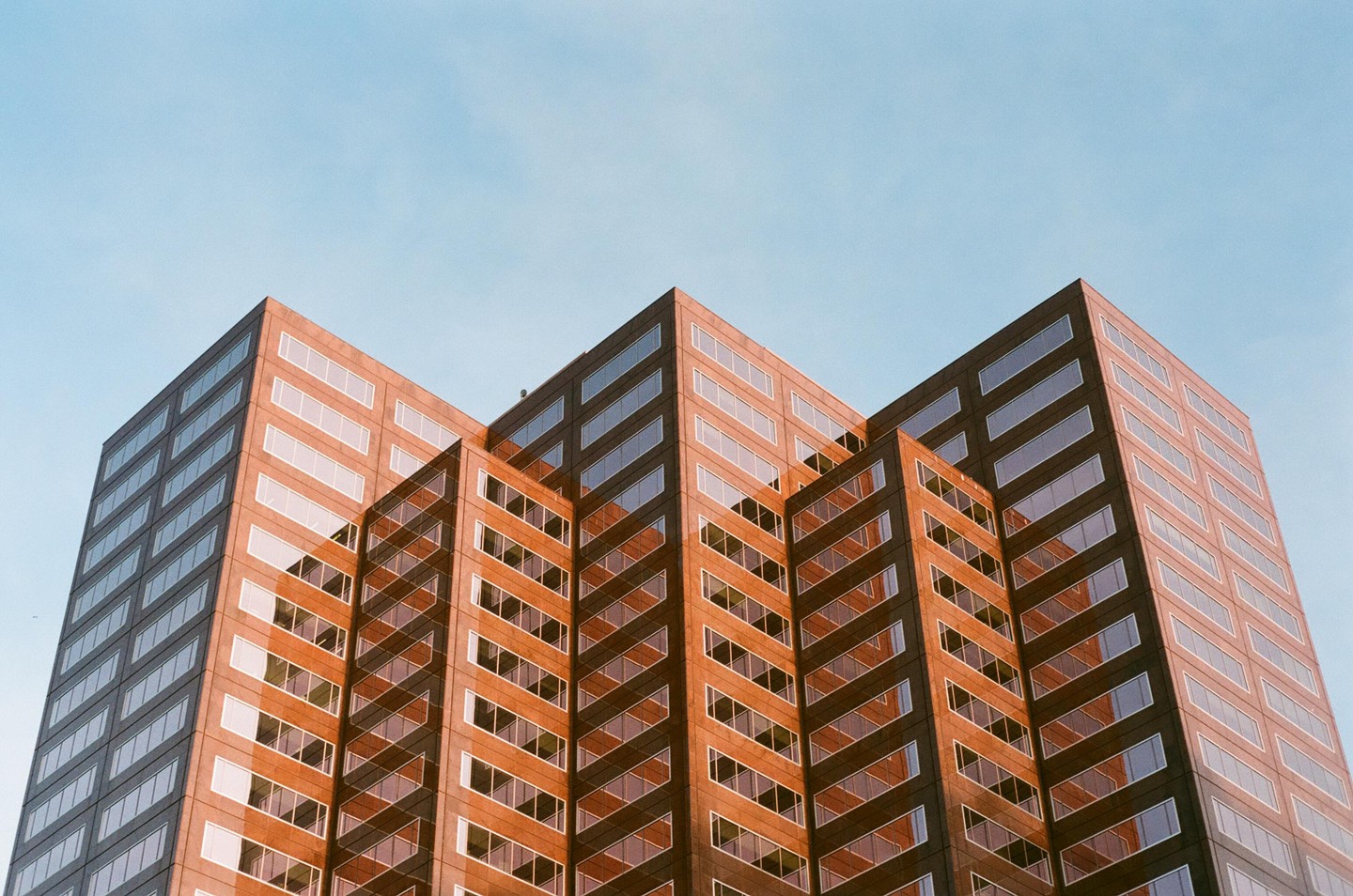 A tall building with many windows is photographed from a low angle against a clear sky.