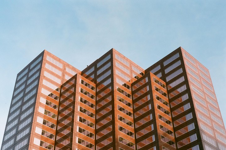 A tall building with many windows is photographed from a low angle against a clear sky.