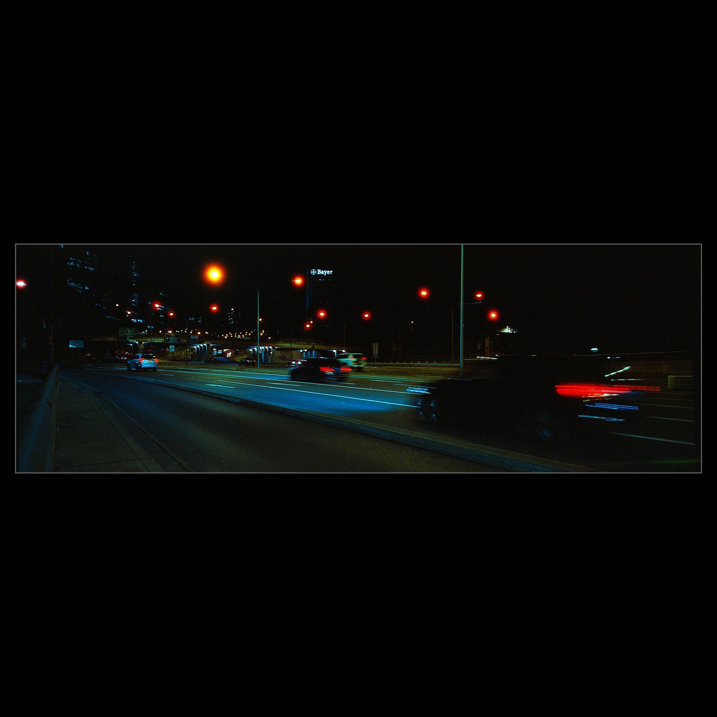Cars drive on a freeway at night, with a "Bayer" sign visible in the distance.