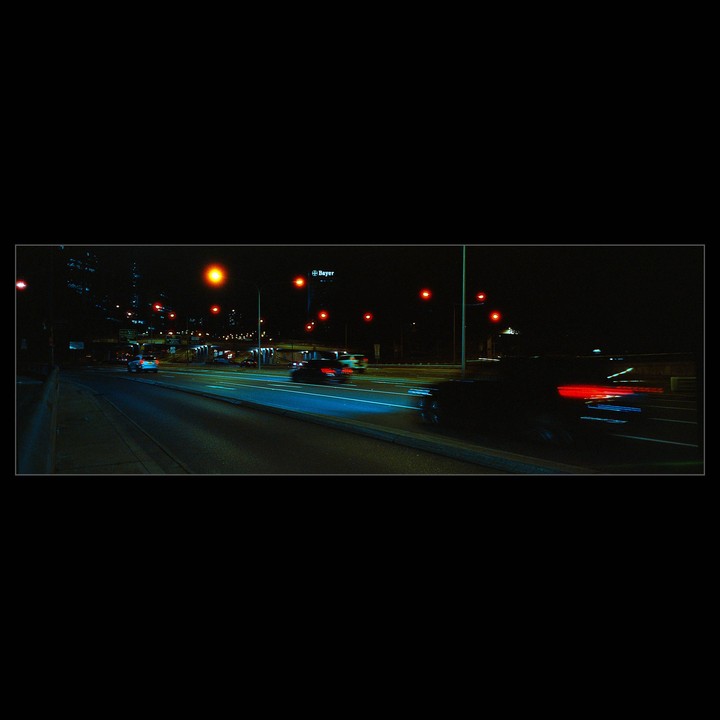 Cars drive on a freeway at night, with a "Bayer" sign visible in the distance.