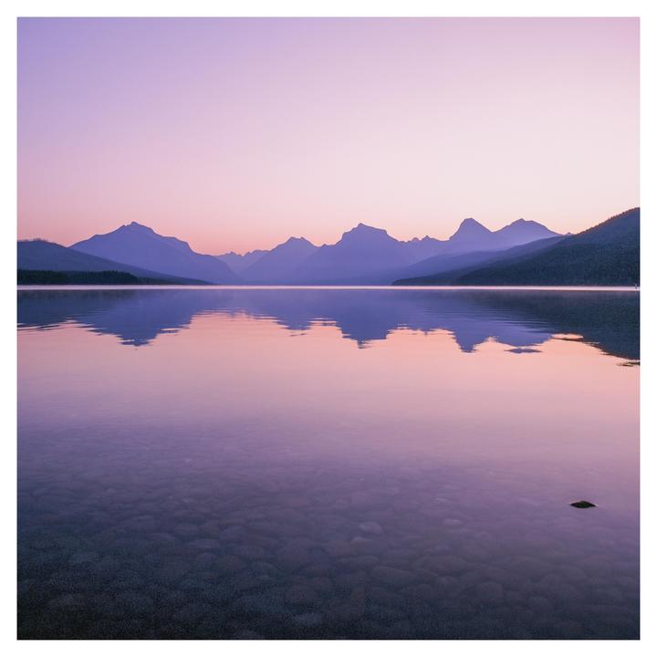 A mountain range is reflected in a calm lake under a pink and purple sky.