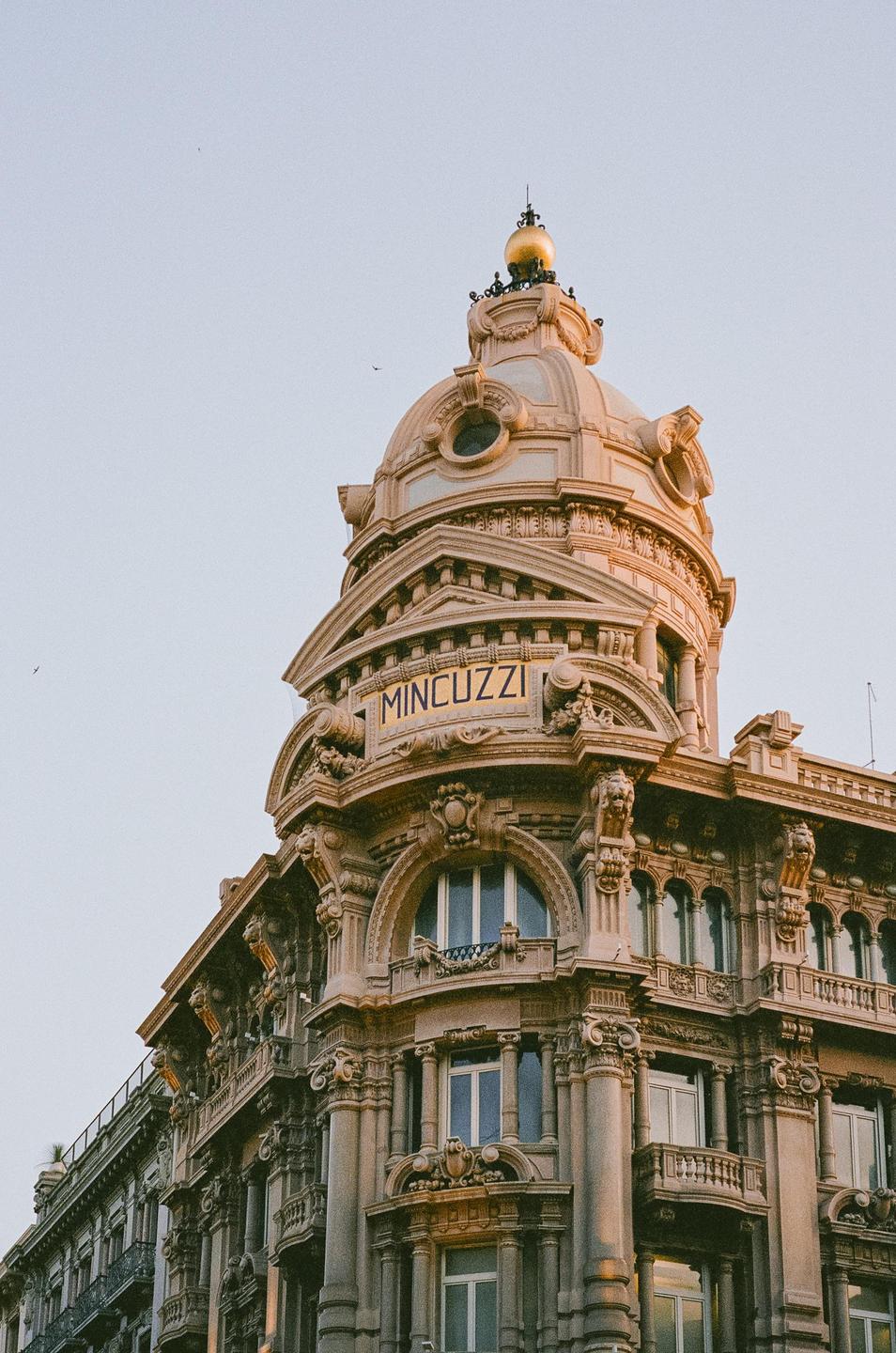 A grand building with a domed roof and ornate carvings stands against a clear sky.
