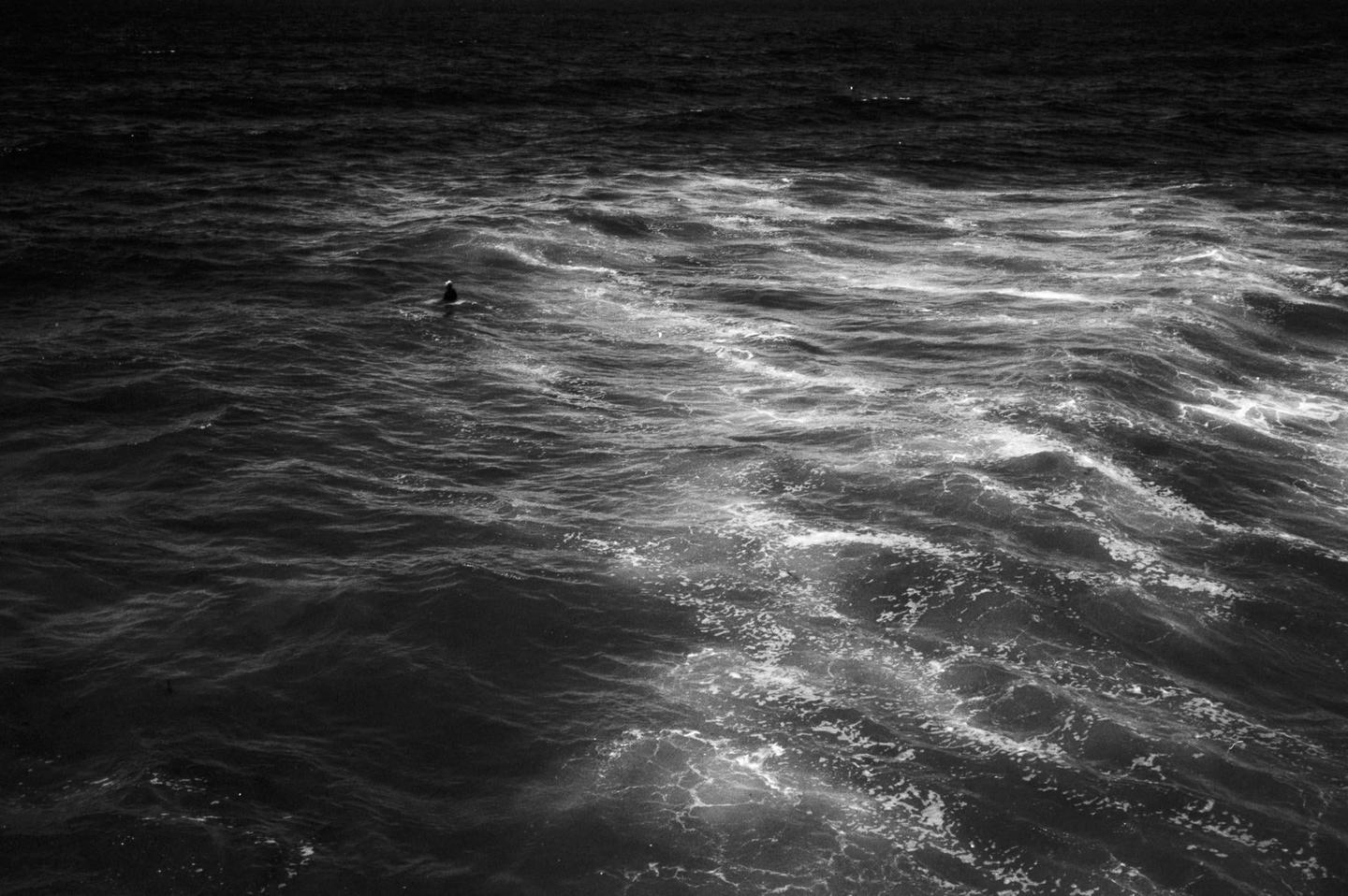 A person sits on a surfboard in the ocean, surrounded by waves.