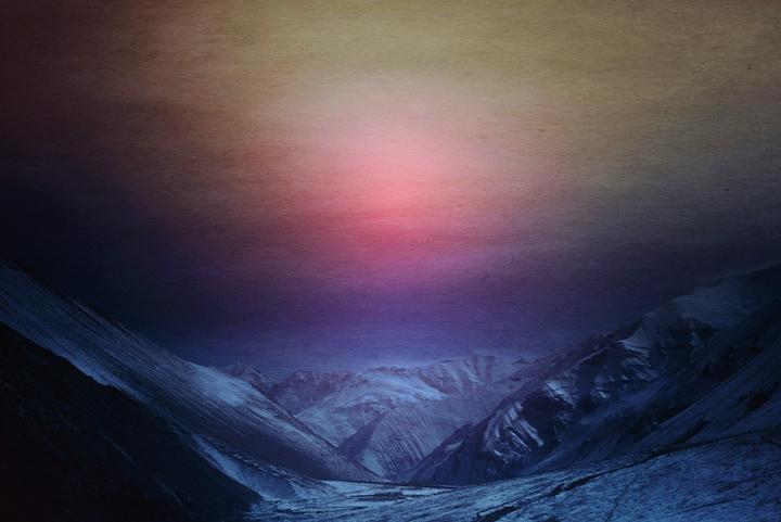 A valley with snow-covered mountains is visible under a colorful sky.