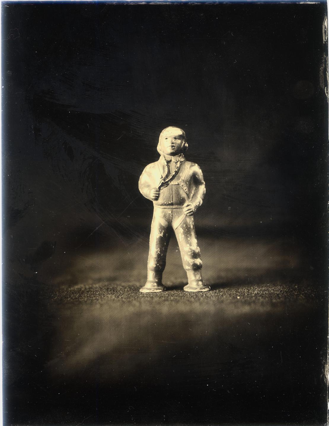 A small, worn figurine of a person in a jumpsuit stands against a dark background.