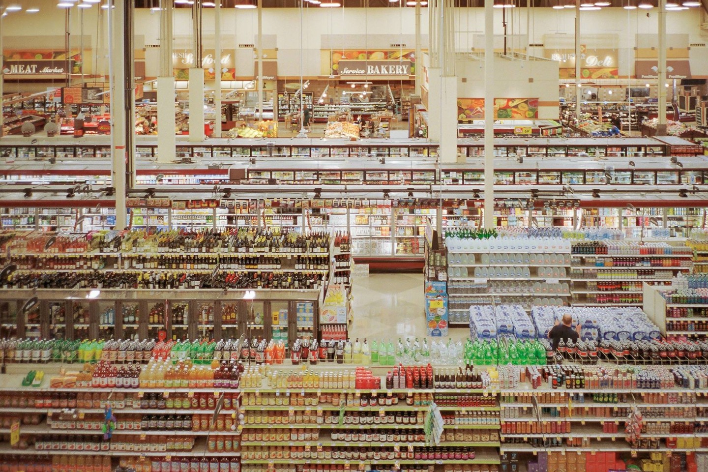 An overhead shot shows a grocery store with many aisles of products and a man stocking shelves.