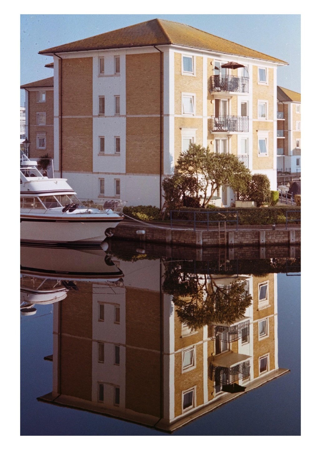 A building with balconies and a boat are reflected in the water of a marina.