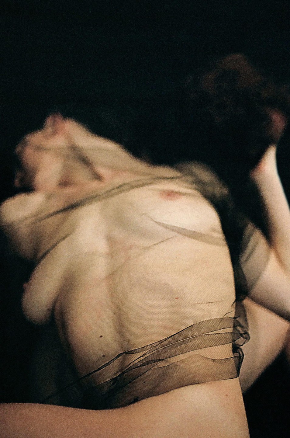 A woman's torso is draped with sheer black fabric against a dark background.