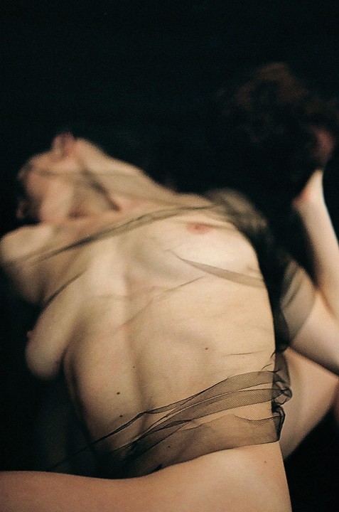 A woman's torso is draped with sheer black fabric against a dark background.