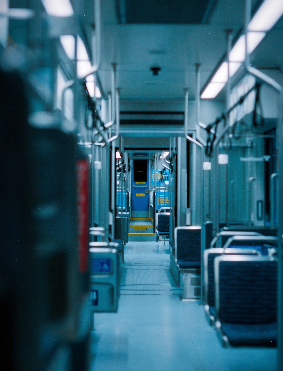 The interior of an empty train car is visible, with rows of seats and handrails leading to a door at the far end.