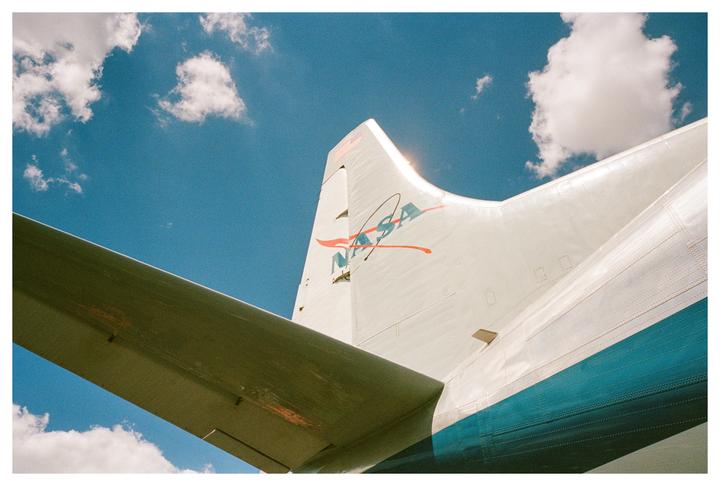 A NASA airplane is shown from the side with a bright blue sky and white clouds in the background.